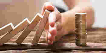 Close-up Of A Businesswoman's Hand Stopping The Wooden Blocks From Falling On Stacked Coins